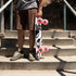 A person standing on concrete stairs holding a longboard skateboard with a black, white, and gray graphic design and bright pink wheels.