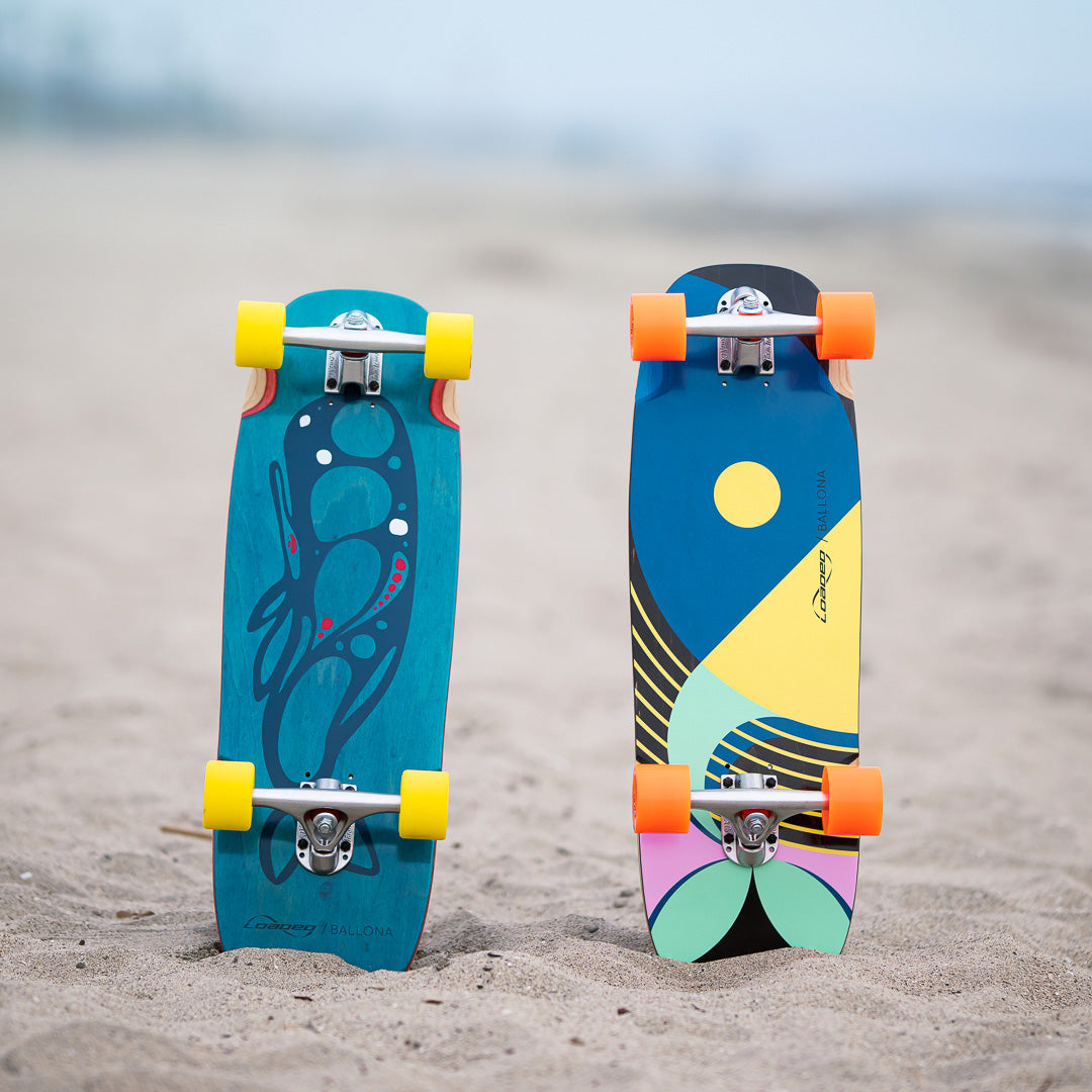 Two colorful skateboards on a sandy surface with a blurred background
