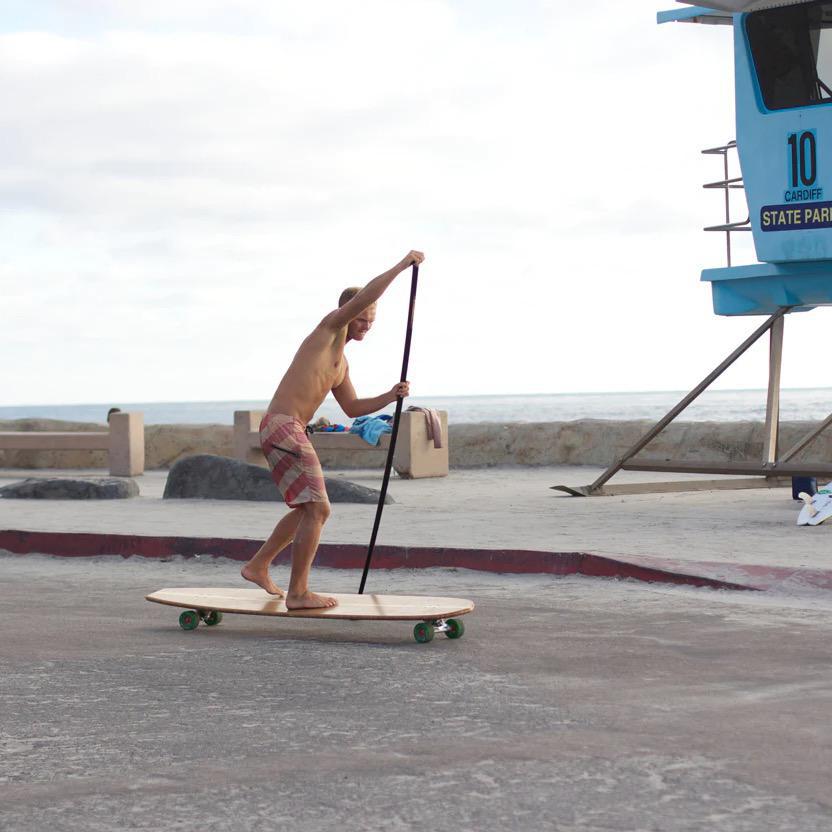 A shirtless man paddling on a longboard near the ocean.