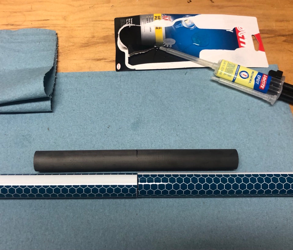 A surface with a ruler, a black cylindrical object, a cleaning brush, and a blue cloth.