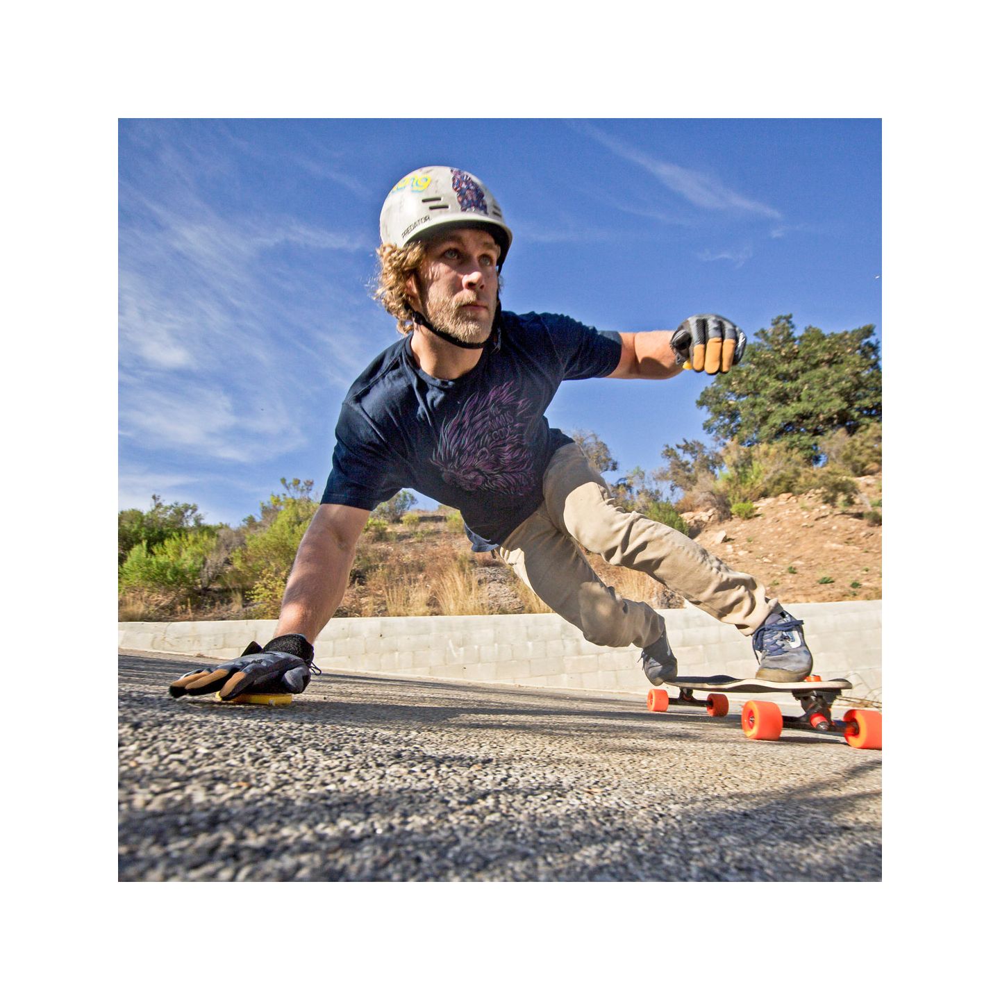 A skateboarder performing a trick on a downhill road with a focused expression.